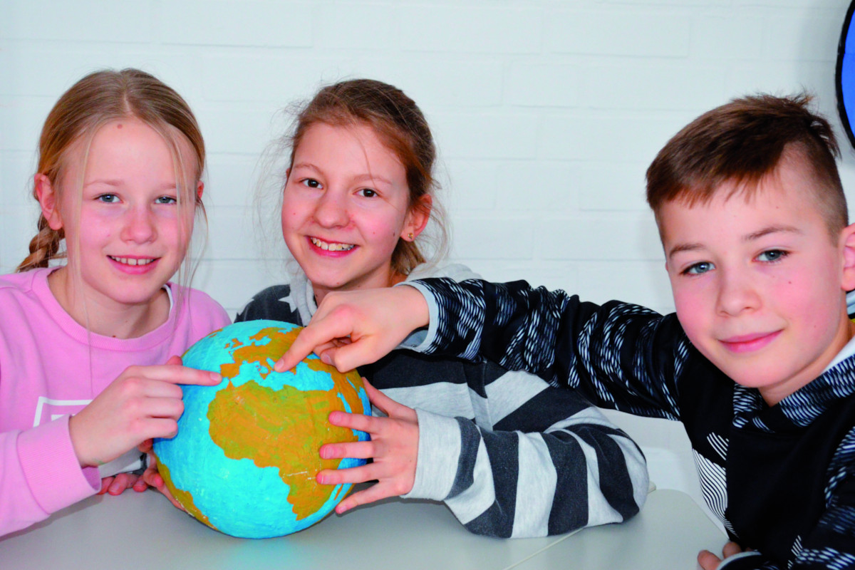 Drei Schüler zeigen mit ihren Finger auf einen Globus