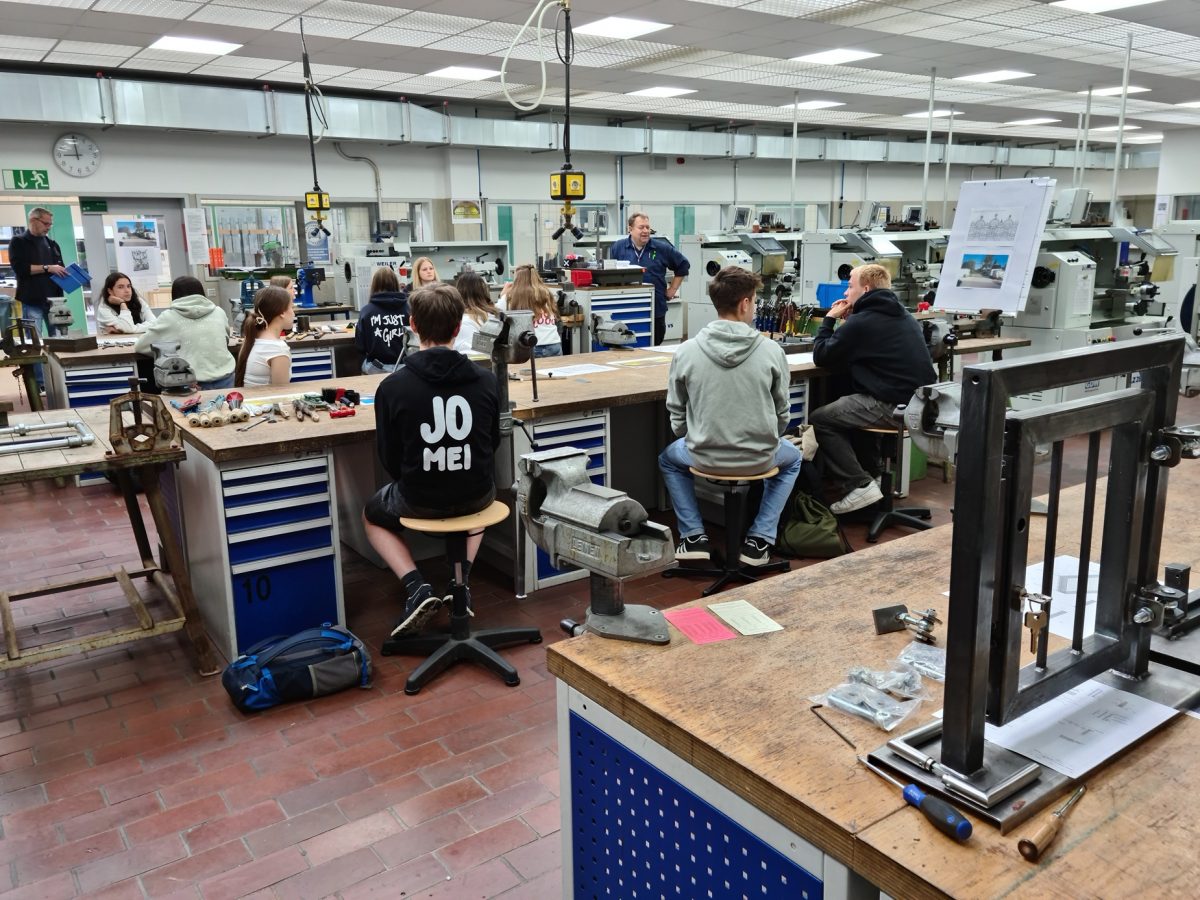 Eine Gruppe Schüler sitzt in einer Werkstatt und lauscht einem Vortrag