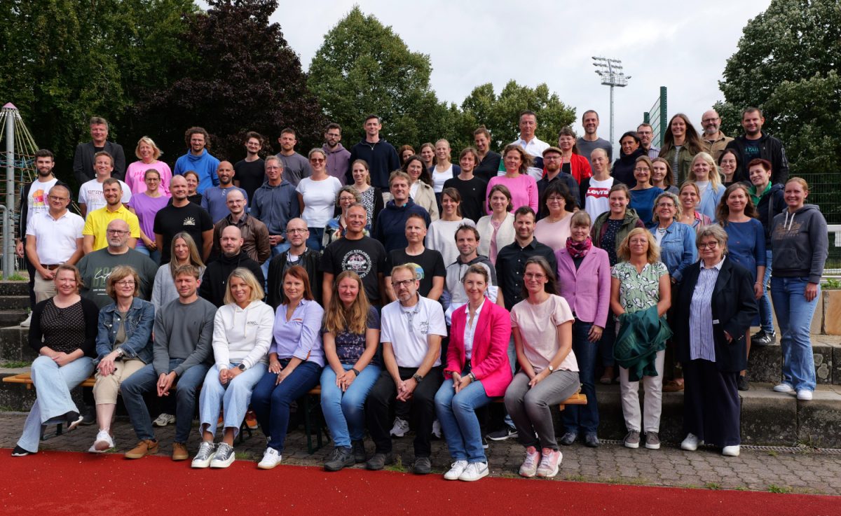 Das Lehrerkollegium steht auf einer Treppe draußen im Schulhof